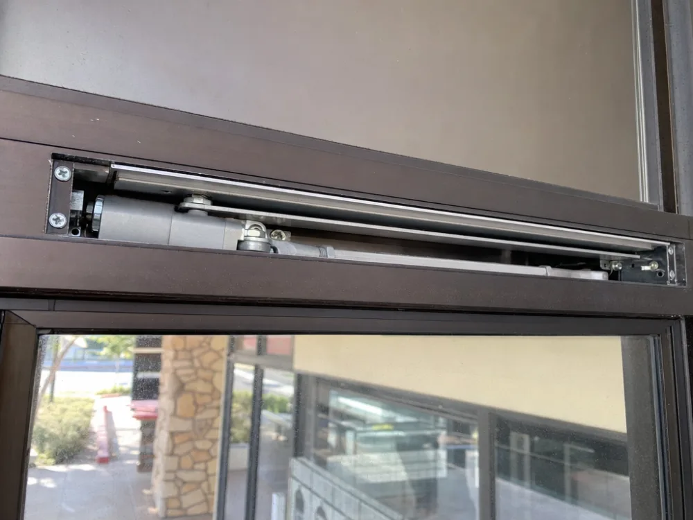 Concealed overhead door closer installed inside the top rail of a glass storefront door