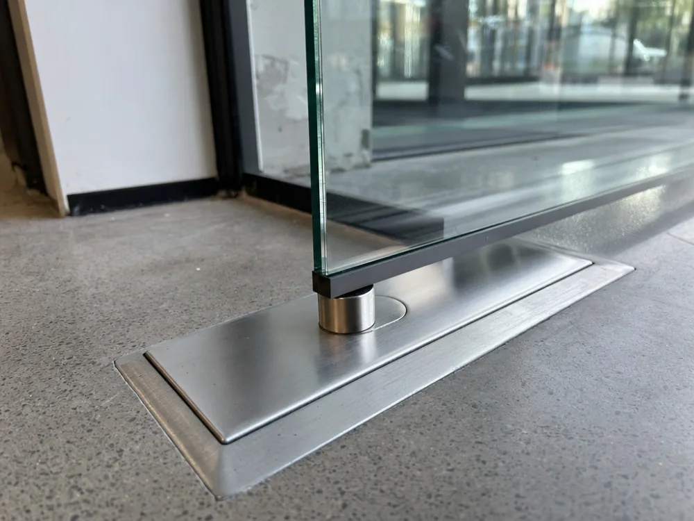 Floor-spring door closer recessed into the floor beneath a heavy glass pivot door